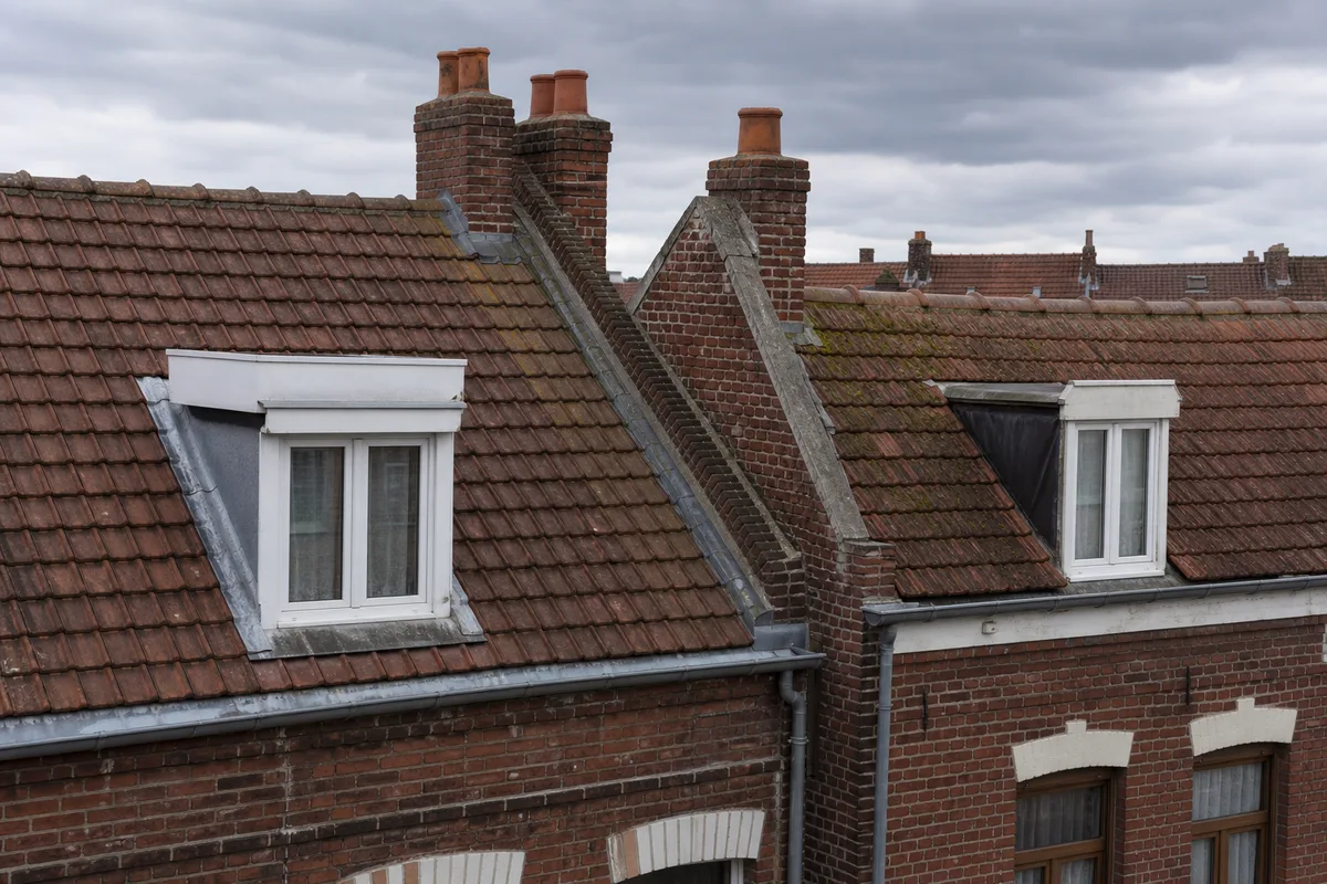 Toits de tuiles rouges et lucarnes de maisons 1930 à Wasquehal sous un ciel gris